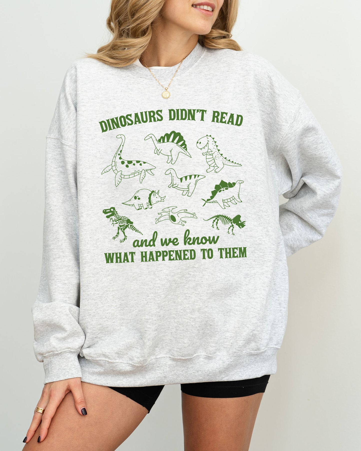 Model wearing ash color sweatshirt with 'Dinosaurs Didn't Read And We Know What Happened To Them' graphic design