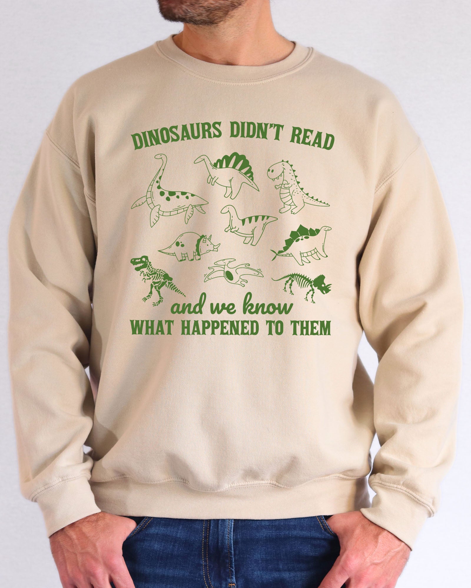 Model wearing sand color sweatshirt with 'Dinosaurs Didn't Read And We Know What Happened To Them' graphic design