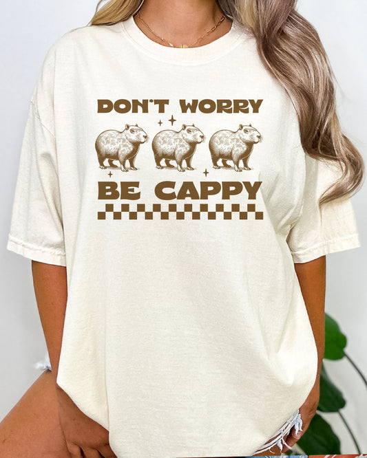 Woman wearing Don't Worry Be Cappy shirt in natural beige color with a cute retro capybara graphic