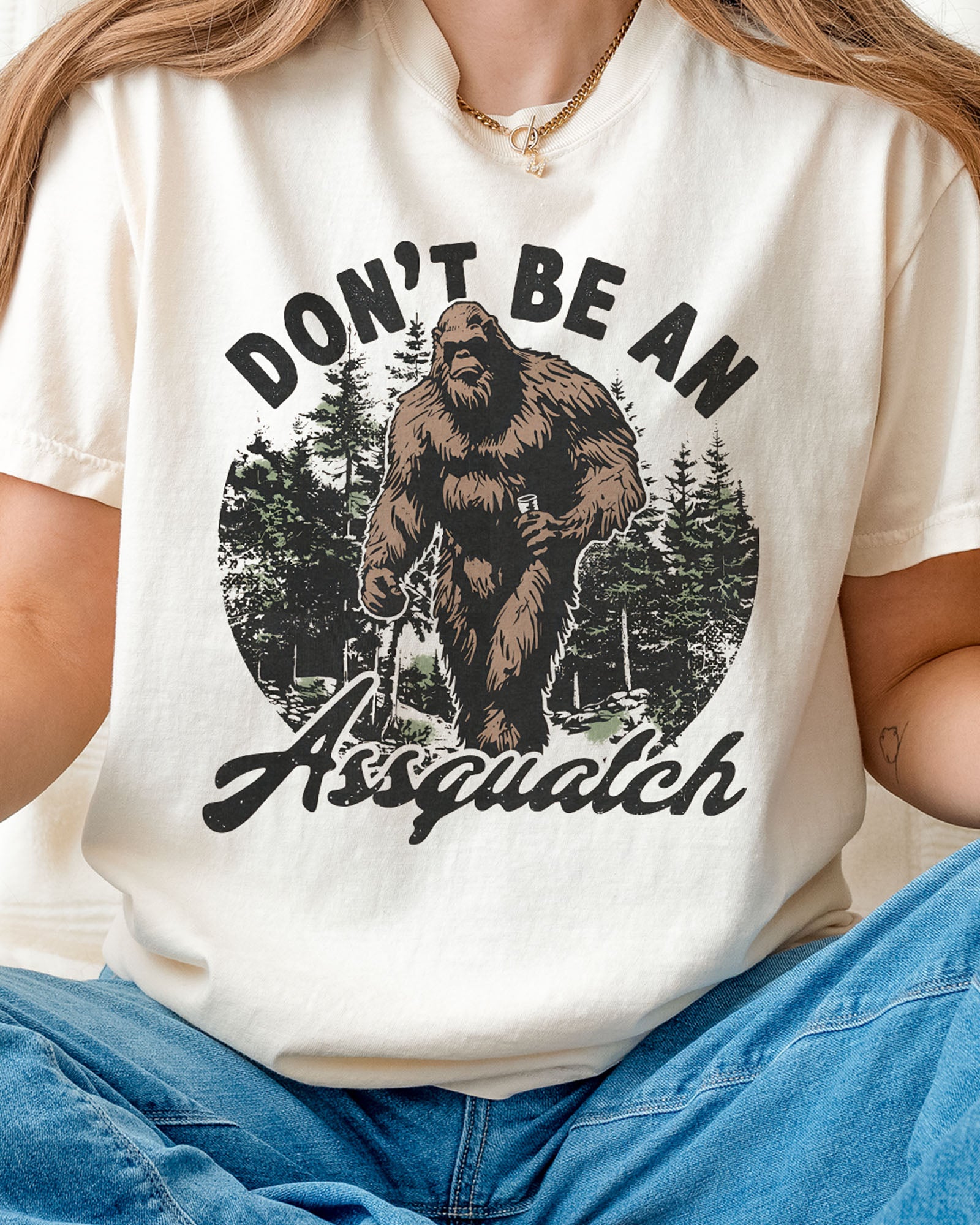 Close-up of woman wearing an ivory "Don't Be an Assquatch" shirt with a funny retro graphic of Bigfoot.