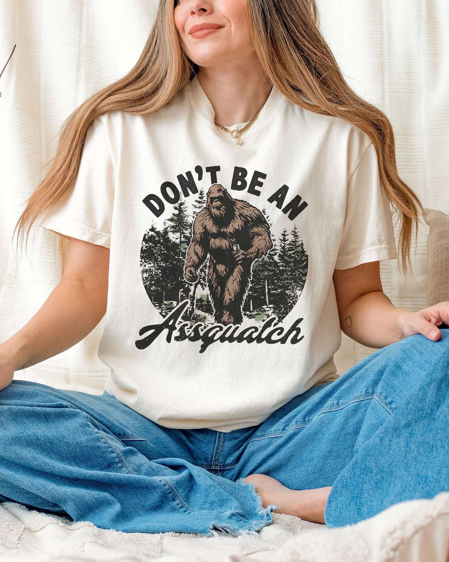 Woman wearing an ivory "Don't Be an Assquatch" shirt with a funny retro graphic of Bigfoot.