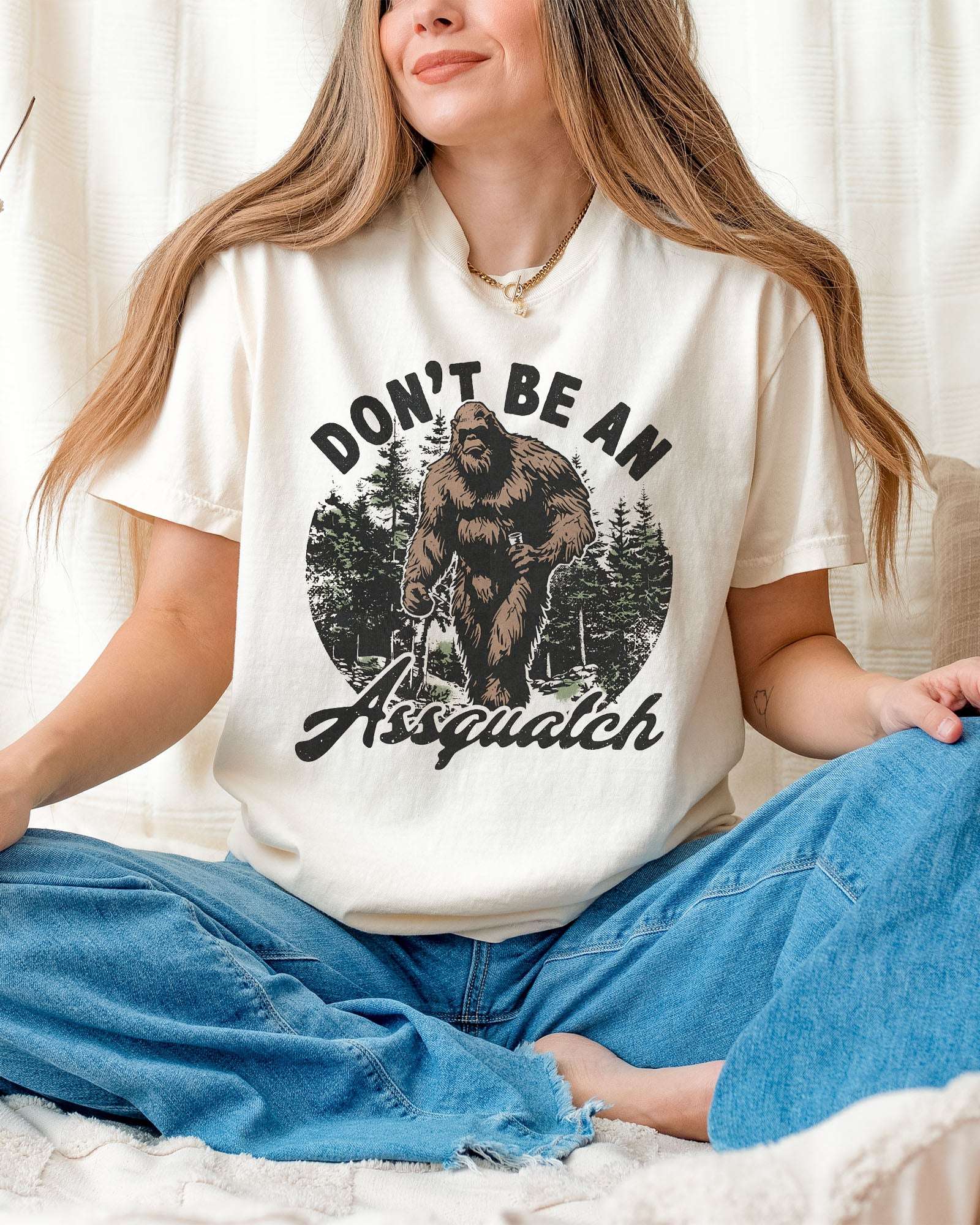 Woman wearing an ivory "Don't Be an Assquatch" shirt with a funny retro graphic of Bigfoot.