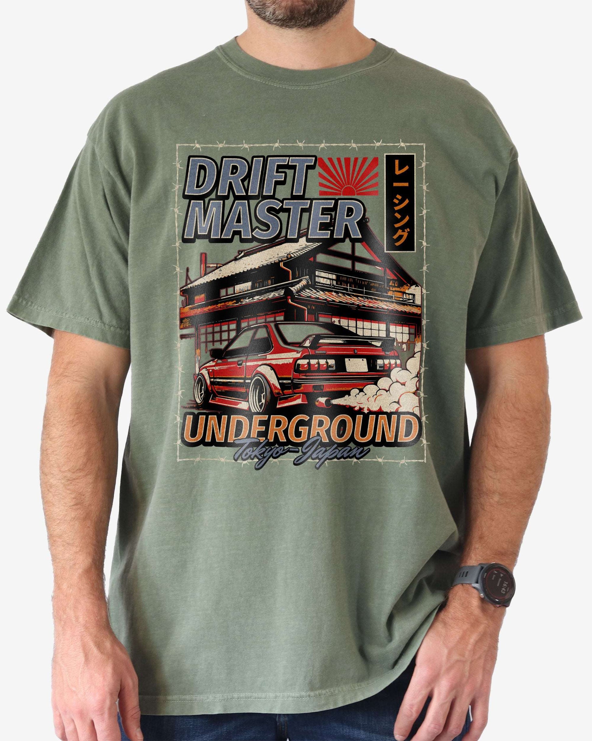 Man wearing a moss Drift Master Tokyo shirt with a retro graphic of a race car and Japanese house.