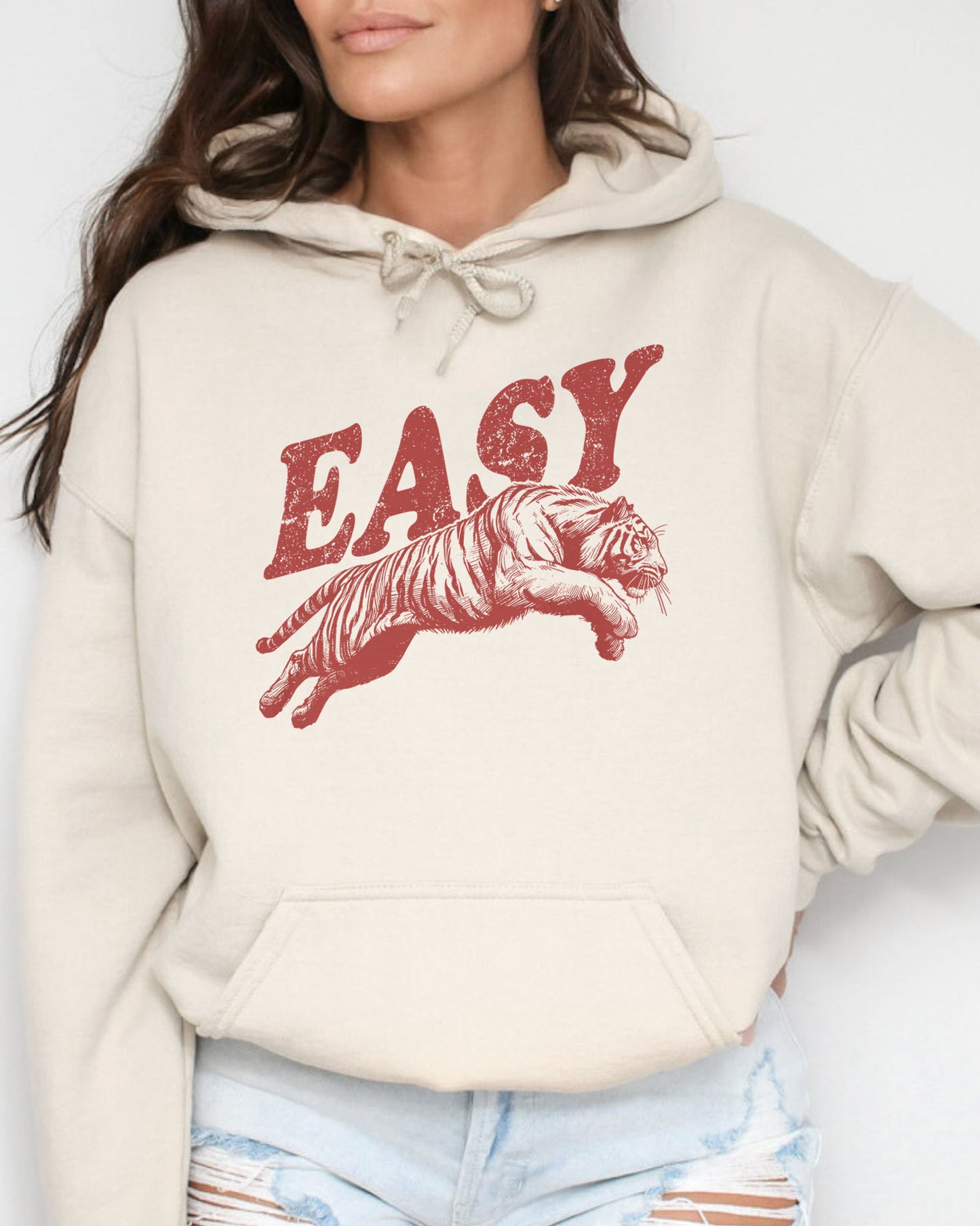 Woman wearing a sand-colored 'Easy Tiger' hoodie featuring a vintage-style graphic of a tiger mid-jump.