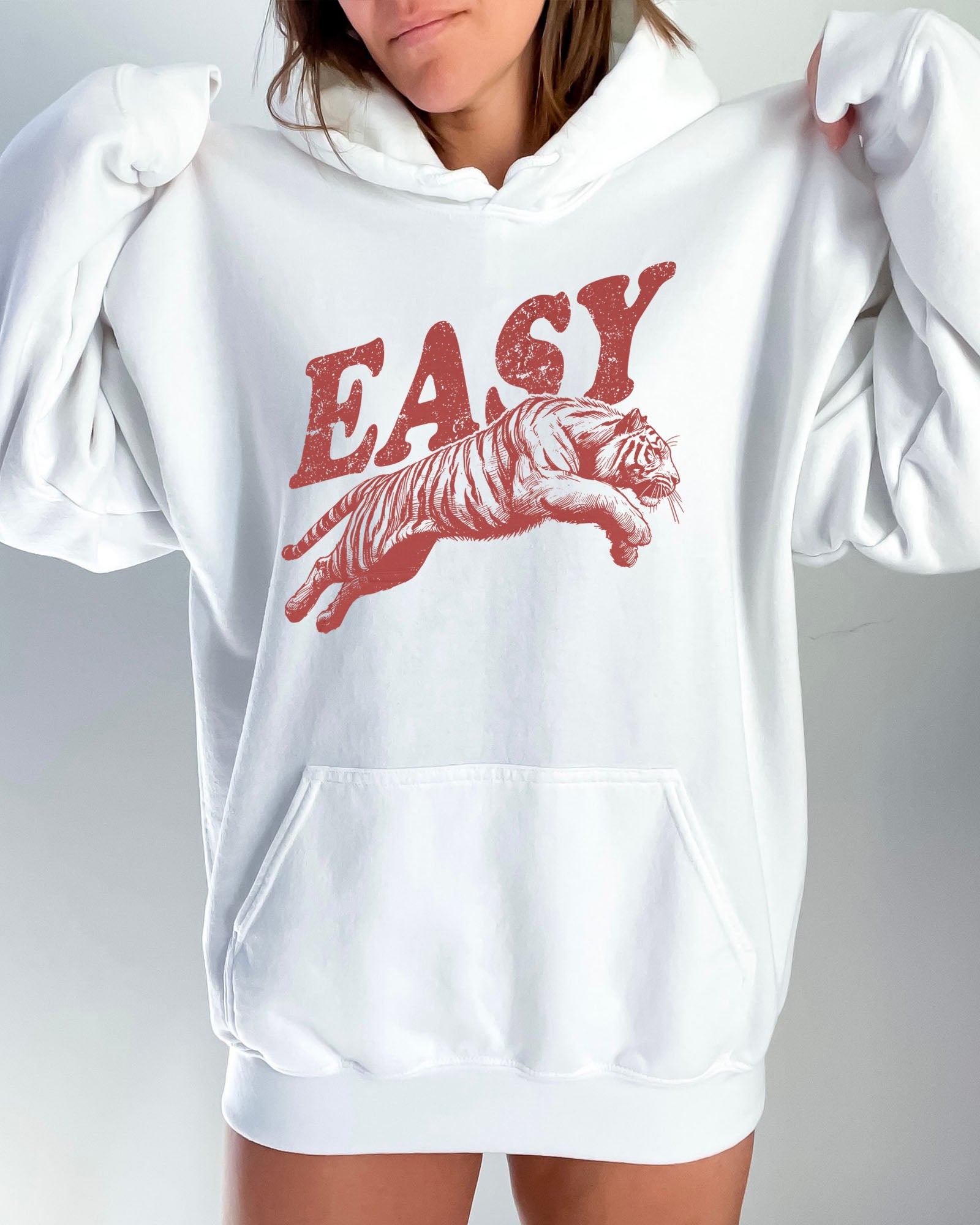 Woman wearing a white-colored 'Easy Tiger' hoodie featuring a vintage-style graphic of a tiger mid-jump.