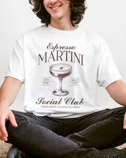 Man wearing a white 'Espresso Martini Social Club – Stirred, Shaken, and Awake' shirt with a retro graphic of an espresso martini glass.