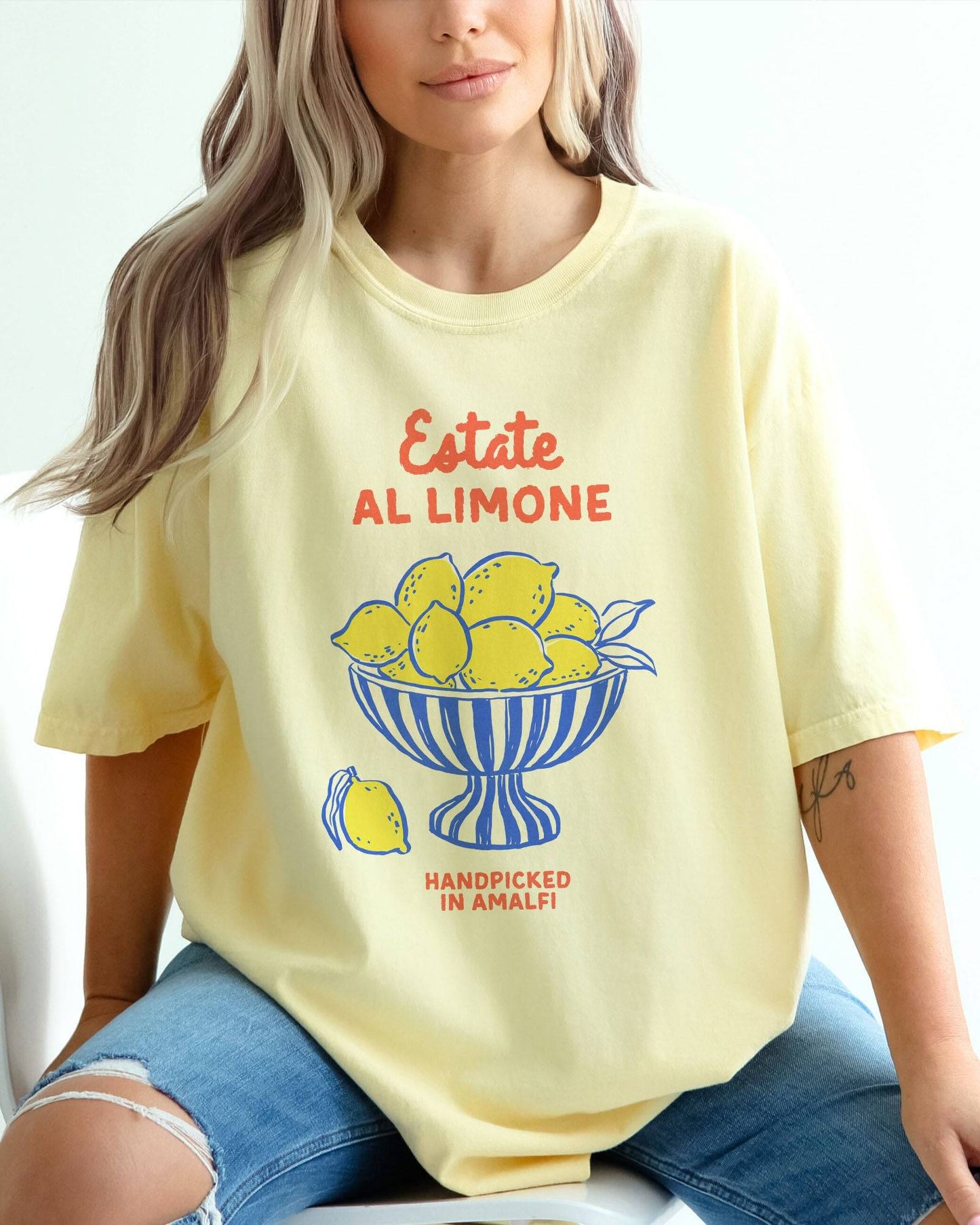 Woman wearing a banana-colored “Estate Al Limone - Handpicked in Amalfi” shirt with a retro graphic of a fruit bowl filled with lemons.