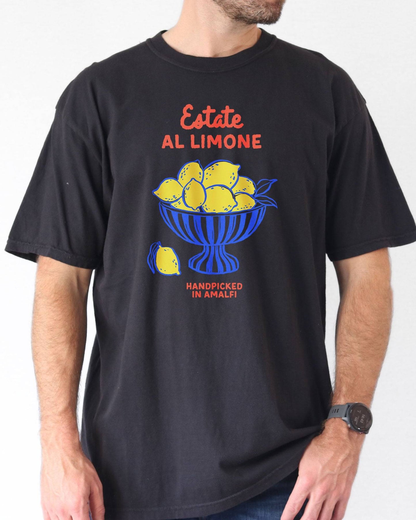 Man  wearing a black “Estate Al Limone - Handpicked in Amalfi” shirt with a retro graphic of a fruit bowl filled with lemons.