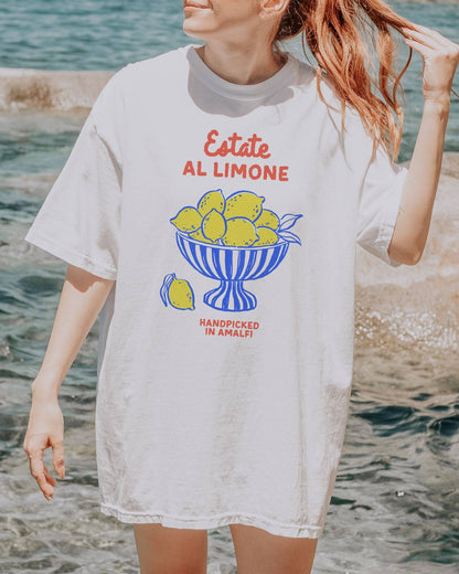 Woman wearing a white “Estate Al Limone - Handpicked in Amalfi” shirt with a retro graphic of a fruit bowl filled with lemons.