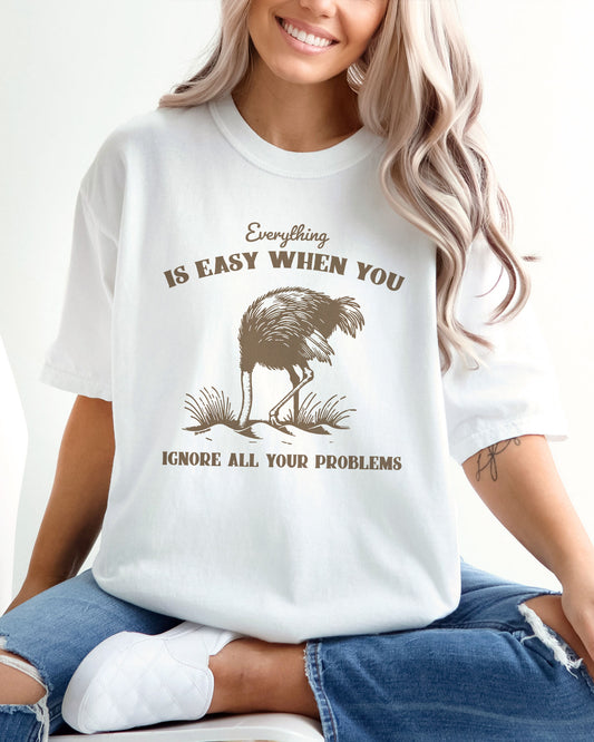 Woman wearing white color shirt with quote "Everything Is Easy When You Ignore All Your Problems" and a retro graphic of a strauss burying his head in the sand.