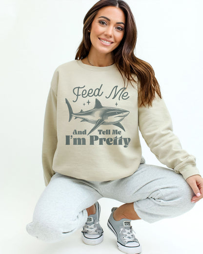 Model wearing sand color sweatshirt with 'Feed Me And Tell Me I'm Pretty' graphic design
