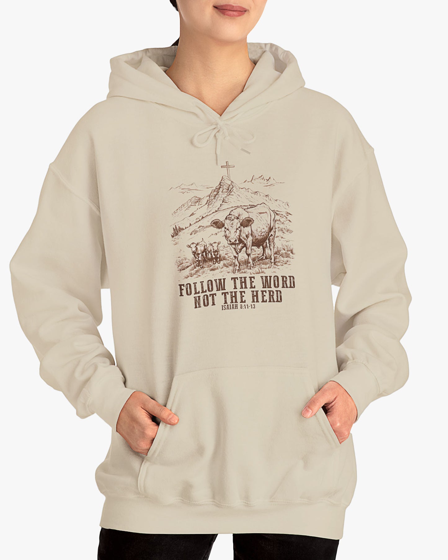 Woman wearing a sand beige 'Follow The Word Not The Herd' hoodie with retro cows and meadow graphic.
