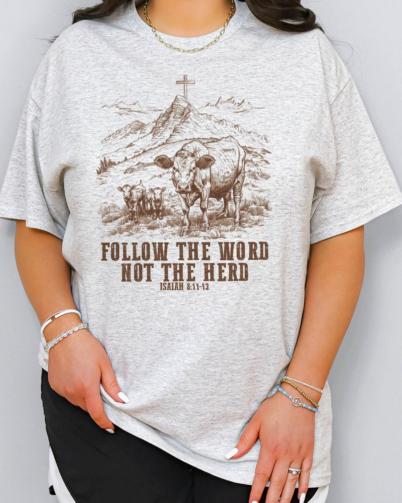 Woman wearing ash grey Christian graphic shirt with Bible verse quote 'Follow the Word, Not the Herd.