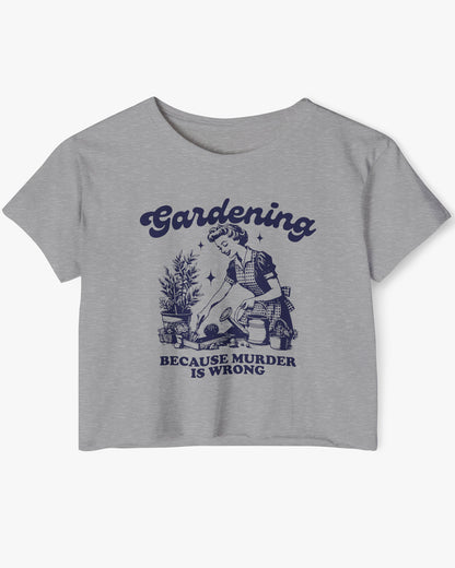 Flat-lay of a dark heather crop top featuring a funny retro-style graphic of a housewife gardening with the text ‘Gardening, Because Murder Is Wrong’.