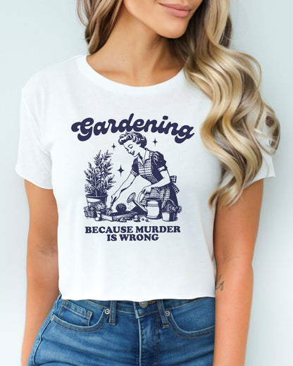 Woman wearing a white crop top with a funny retro-style graphic of a housewife gardening, featuring the text ‘Gardening, Because Murder Is Wrong’.
