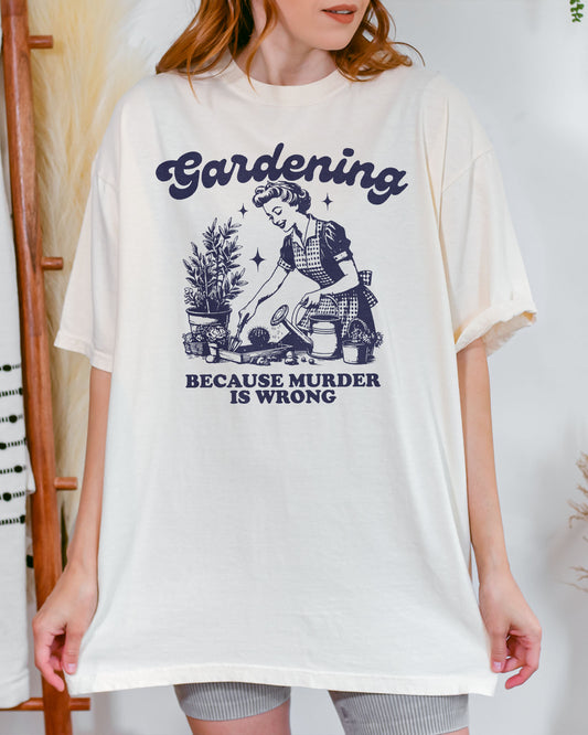 Woman wearing an ivory "Gardening Because Murder Is Wrong" shirt with a funny retro graphic of a housewife gardening in a flower bed.