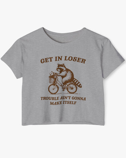 Flat lay dark heather 'Get In Loser, Trouble Ain't Gonna Make Itself' crop top featuring a funny retro raccoon riding a bicycle.