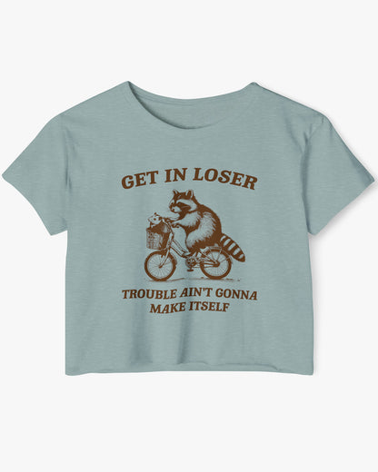 Flat lay stonewash green 'Get In Loser, Trouble Ain't Gonna Make Itself' crop top featuring a funny retro raccoon riding a bicycle.
