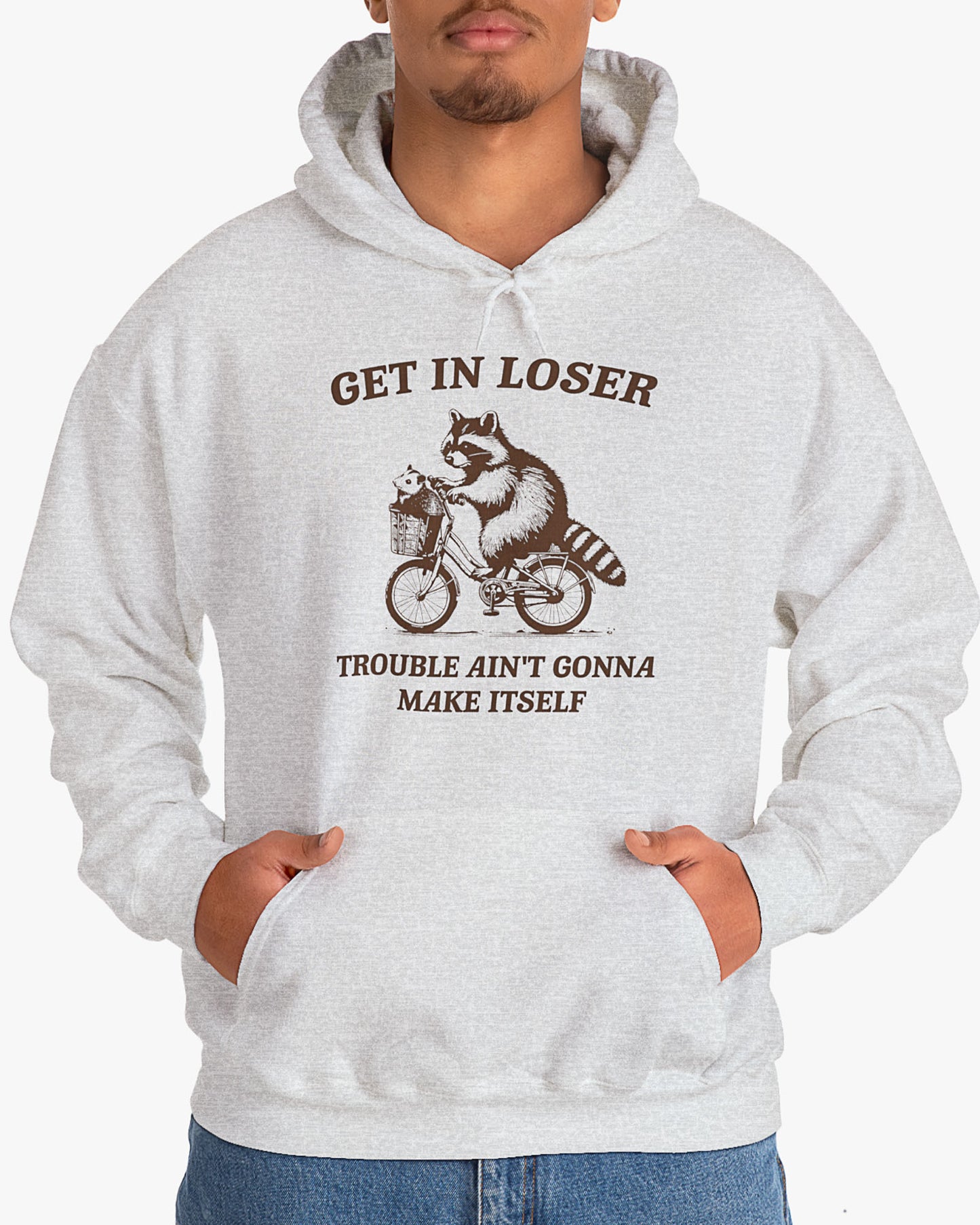 Man wearing ash gray color hoodie with the quote 'Get In Loser, Trouble Ain't Gonna Make Itself' and a funny retro raccoon riding a bycicle graphic