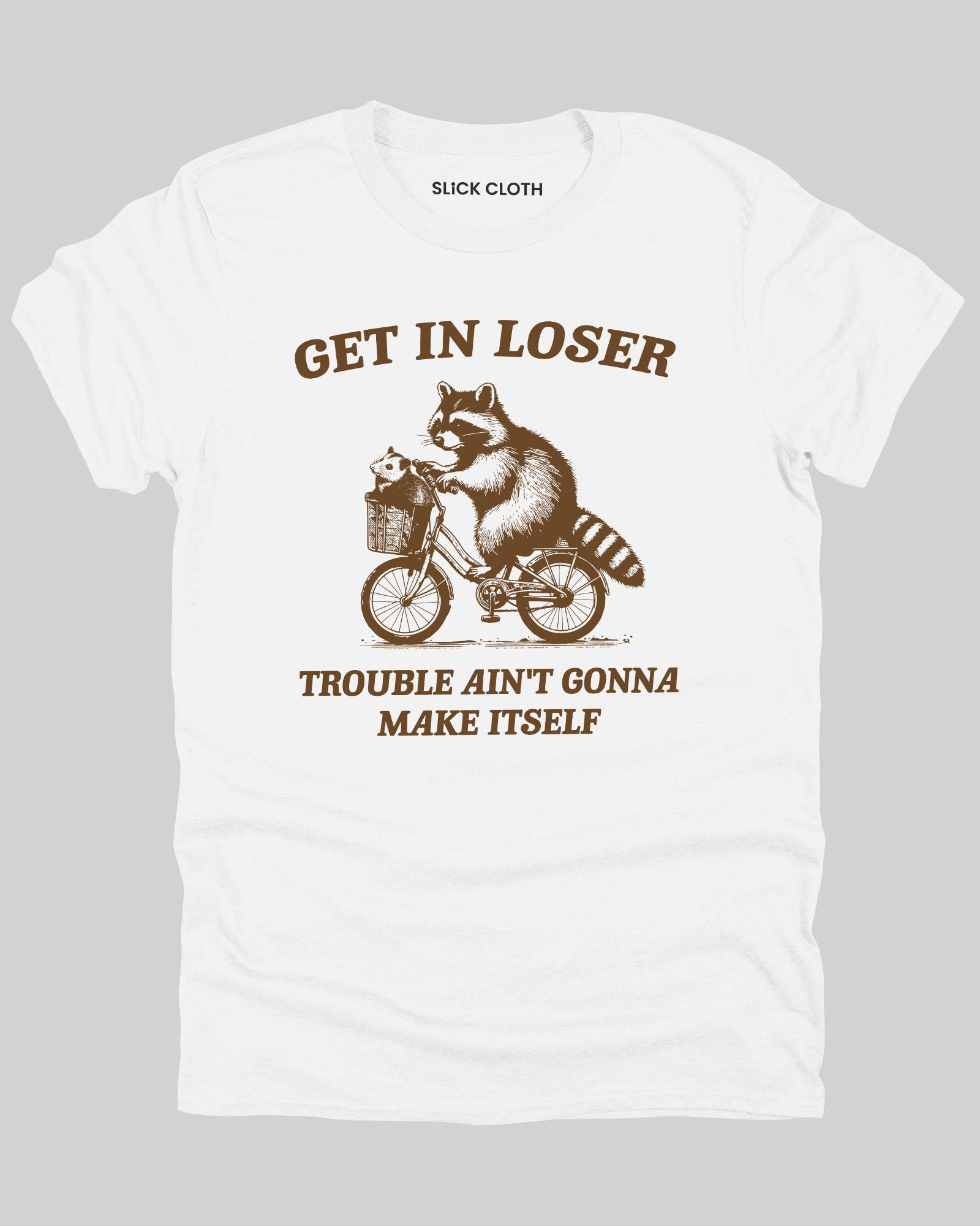 Flat lay white 'Get In Loser, Trouble Ain't Gonna Make Itself' shirt featuring a funny retro raccoon riding a bicycle graphic.