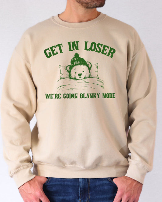 Man wearing a sand beige sweatshirt with a funny retro graphic of a teddy bear in bed and the quote "Get In Loser We're Going Blanky Mode".