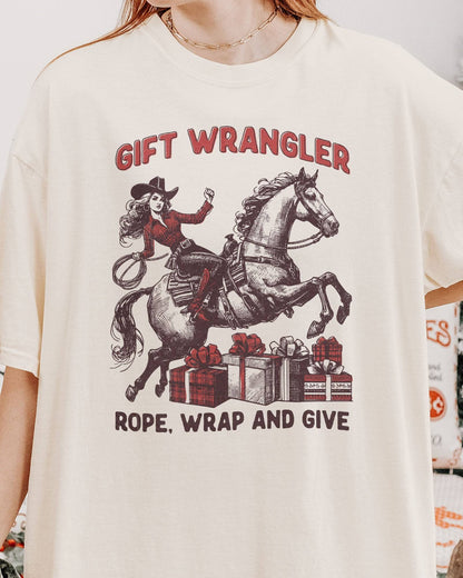 Close-up of woman wearing an ivory "Gift Wrangler – Rope, Wrap and Give" shirt with a funny retro cowgirl Christmas graphic.