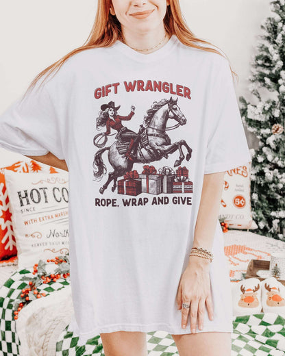 Woman wearing a white "Gift Wrangler – Rope, Wrap and Give" shirt with a funny retro cowgirl Christmas graphic.