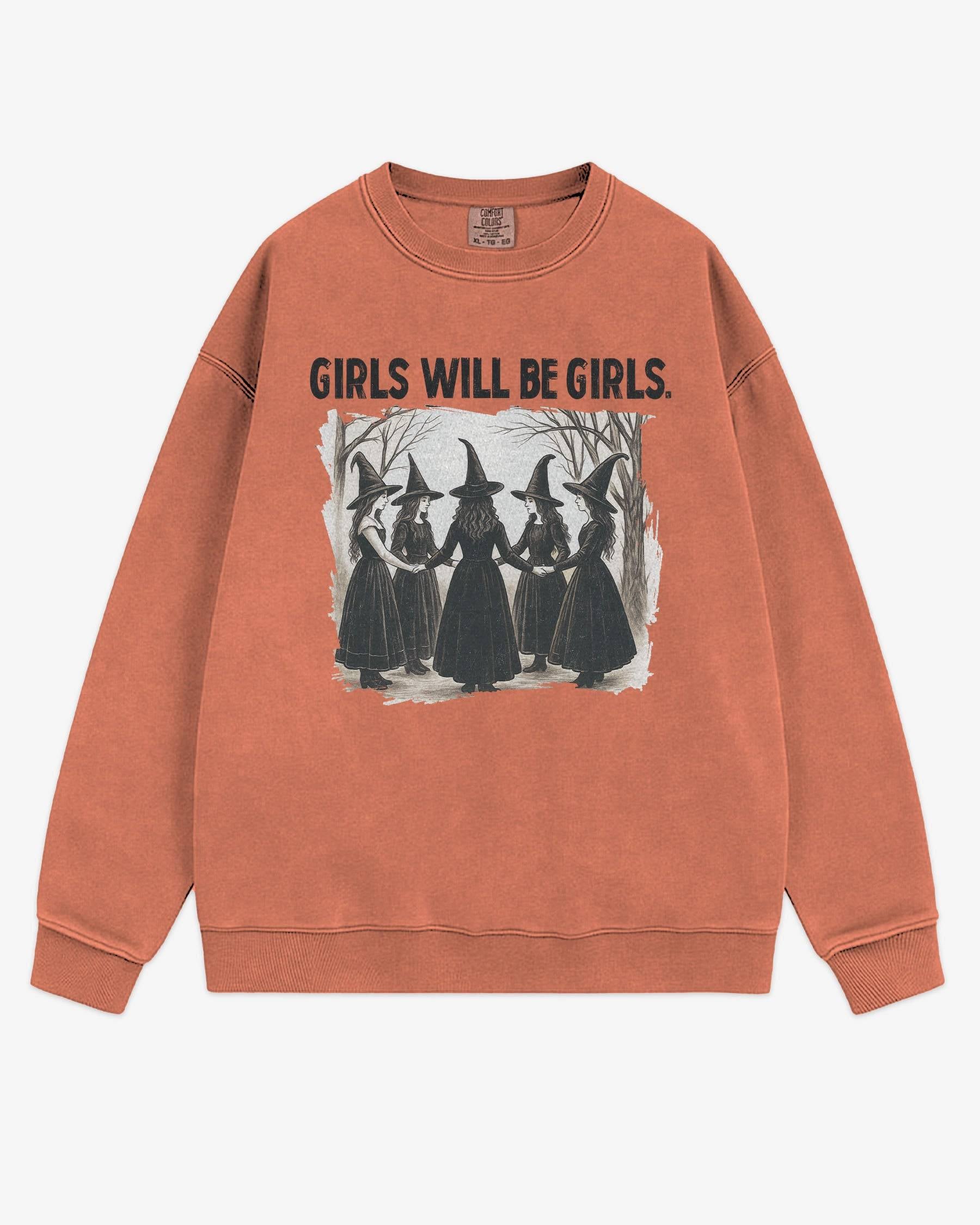Flat lay terracotta 'Girls Will Be Girls' sweatshirt with retro graphic of witches holding hands in a Halloween ritual.