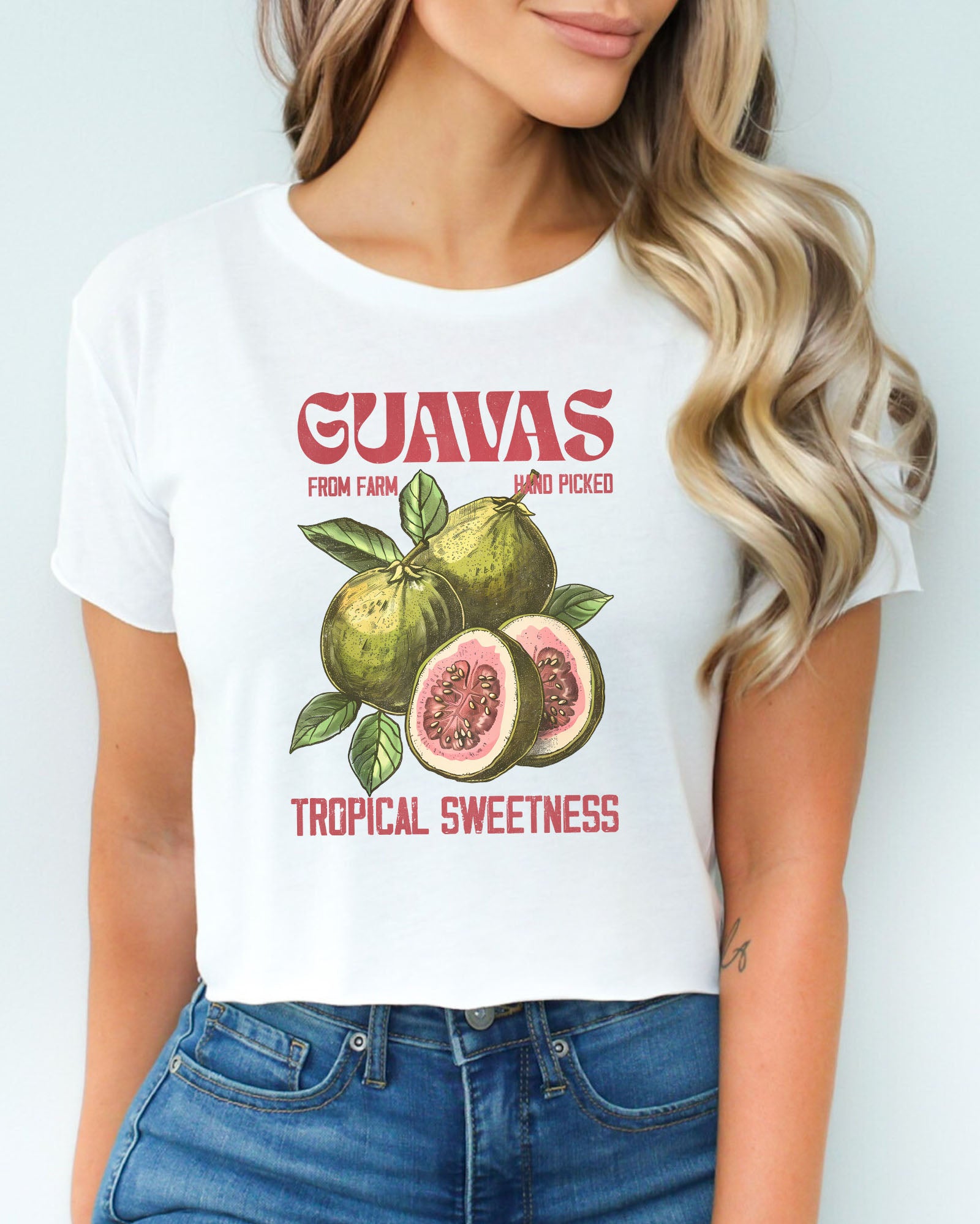 Woman wearing a white crop top with a retro commercial guavas fruit graphic.