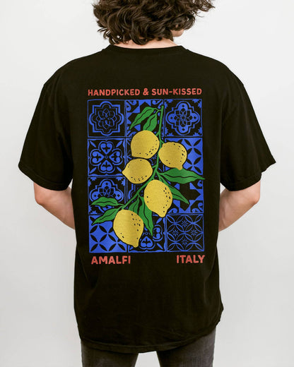 Man wearing a black "Handpicked & Sun-Kissed Amalfi Italy" shirt with a retro graphic of lemons over a floral pattern background.