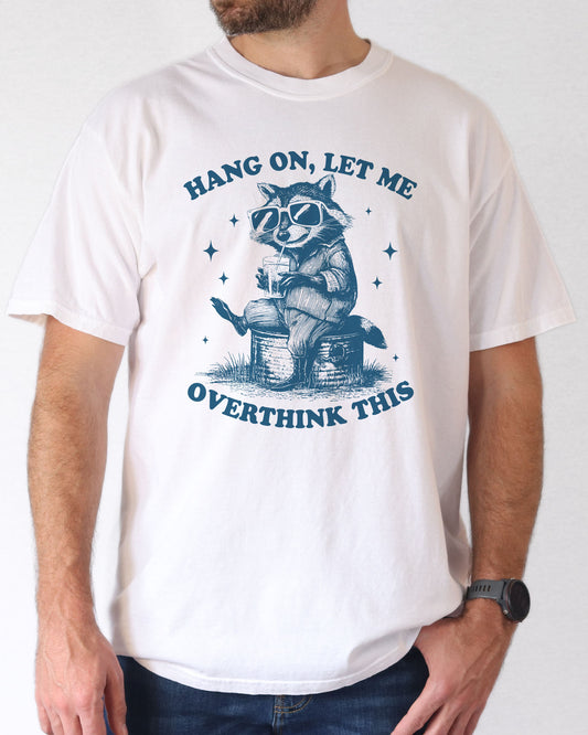 Man wearing white color 'Hang On Let me Overthink This' shirt with funny retro raccoon wearing sunglasses graphic