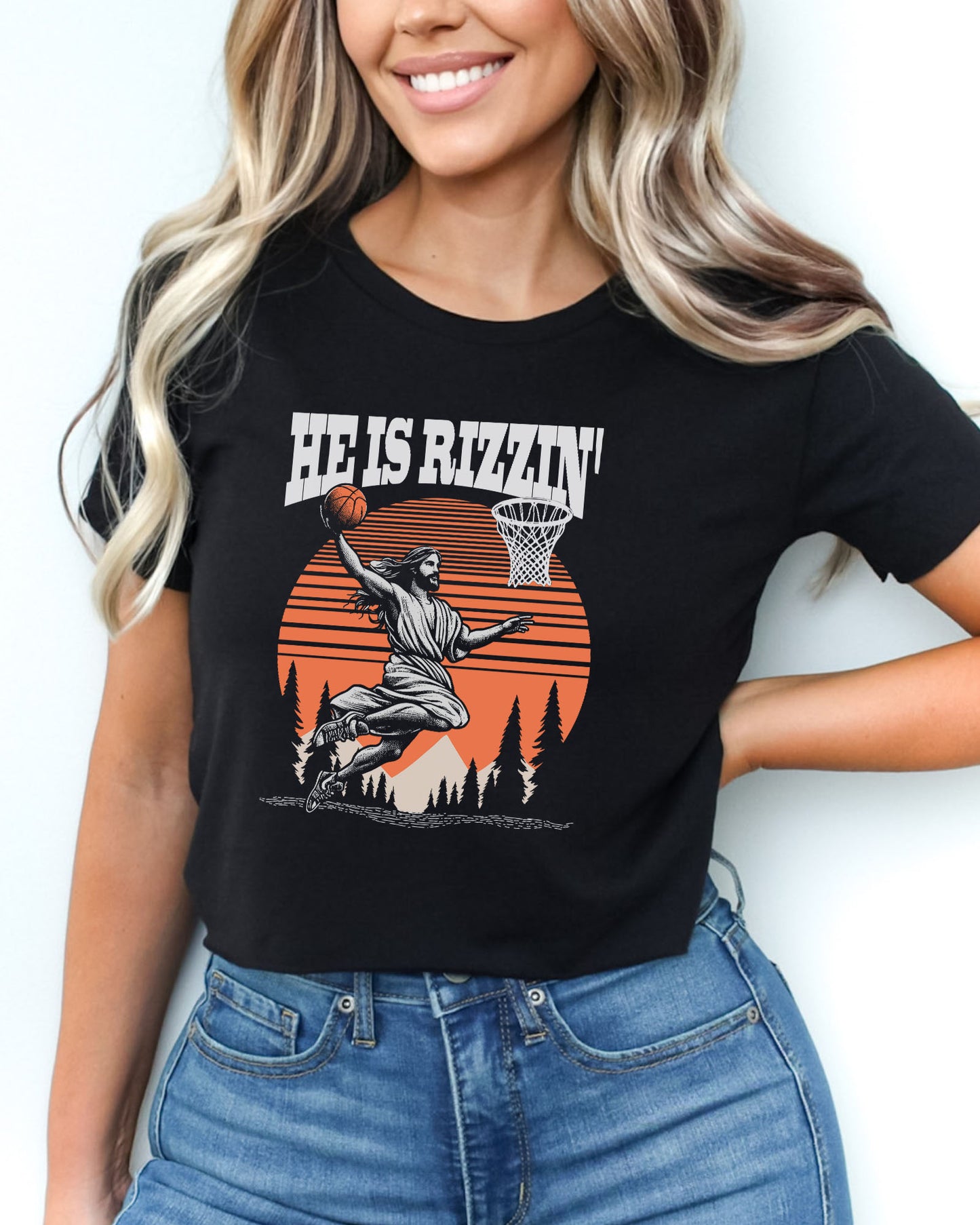 Woman wearing a black 'He Is Rizzin' crop top featuring a funny retro graphic of Jesus slam-dunking a basketball.