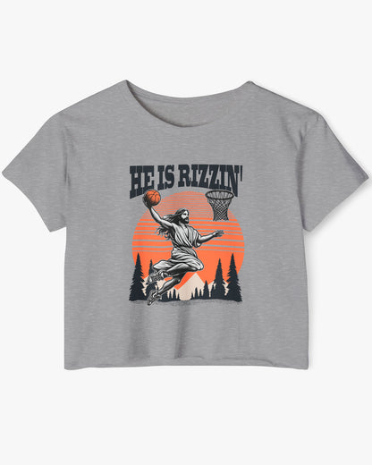 Flat lay of a heather gray 'He Is Rizzin' crop top featuring a funny retro graphic of Jesus slam-dunking a basketball.