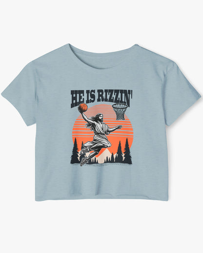 Flat lay of a stonewash denim 'He Is Rizzin' crop top featuring a funny retro graphic of Jesus slam-dunking a basketball.