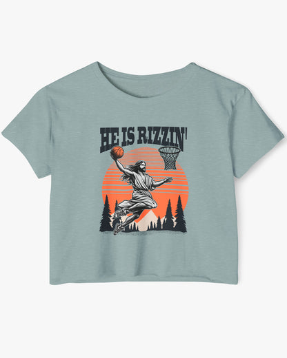 Flat lay of a stonewash green 'He Is Rizzin' crop top featuring a funny retro graphic of Jesus slam-dunking a basketball.