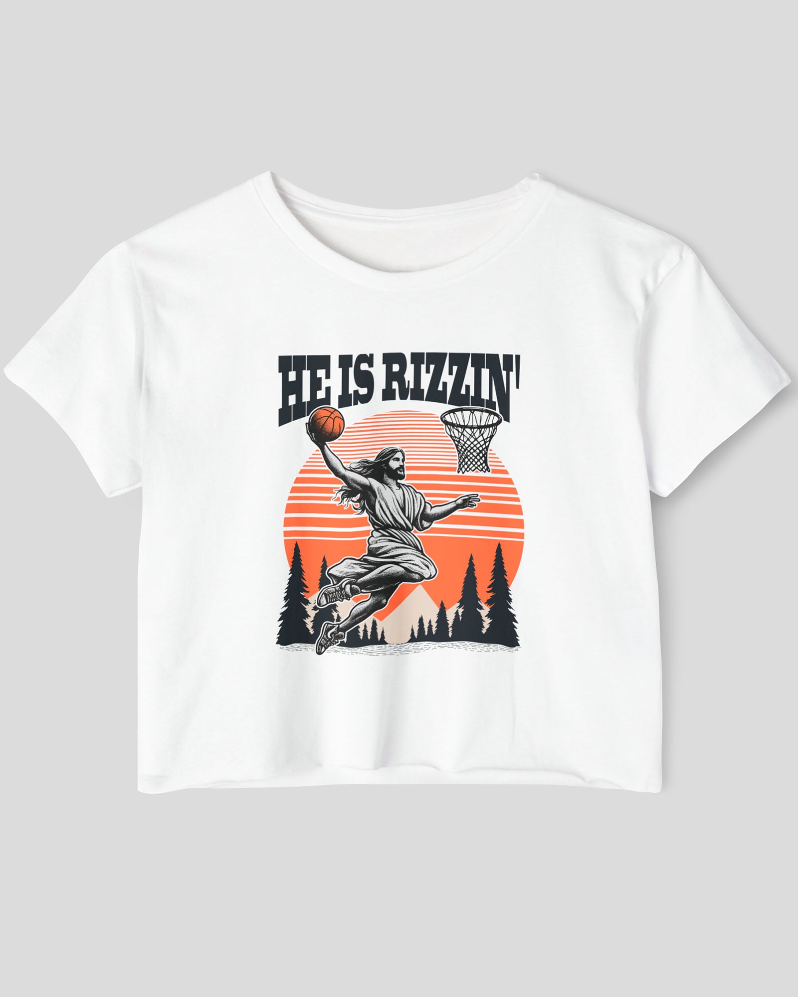 Flat lay of a white 'He Is Rizzin' crop top featuring a funny retro graphic of Jesus slam-dunking a basketball.