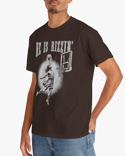 Man is wearing He is Rizzin' tee in dark chocolate color with funny Jesus dunking a basketball graphic
