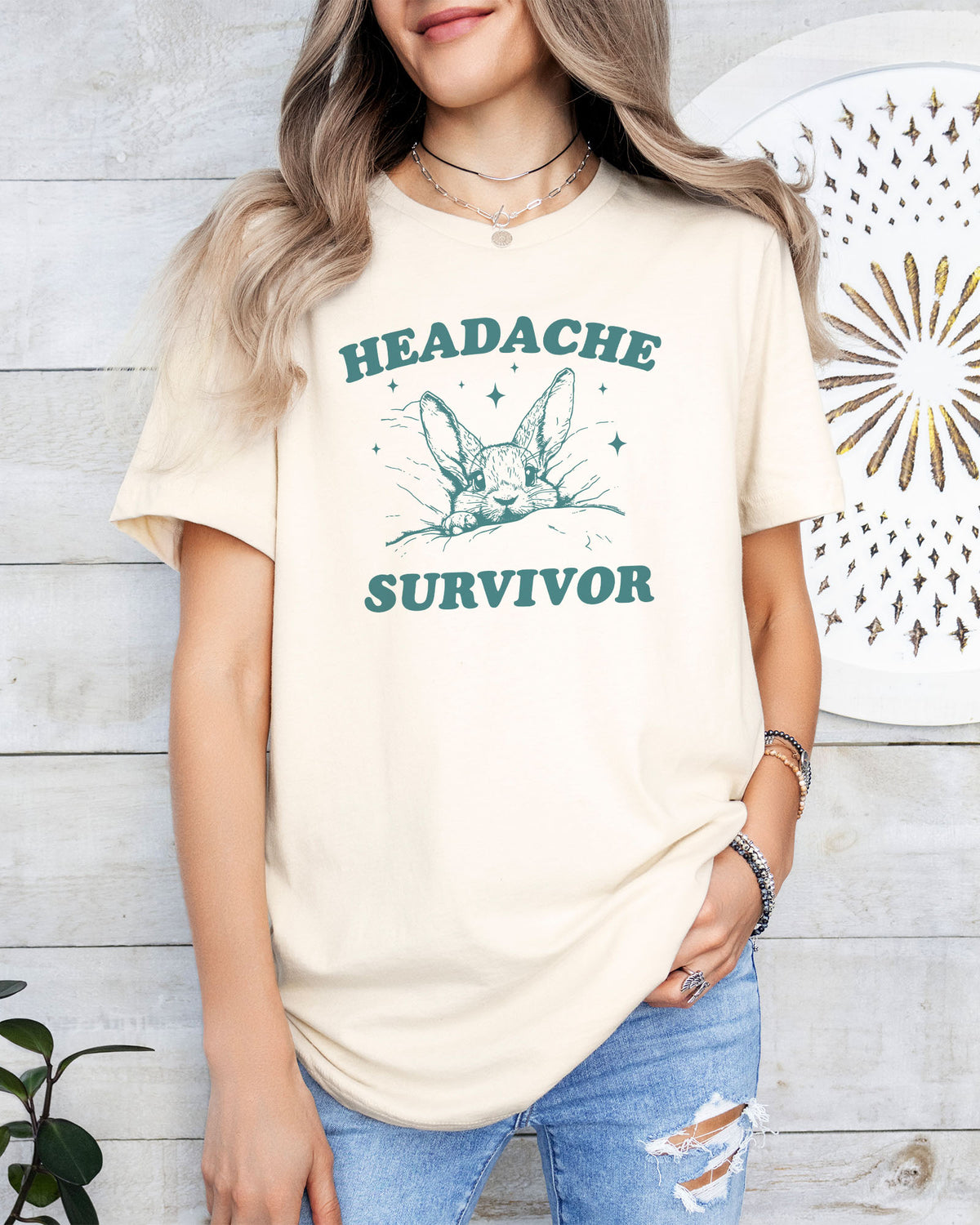 Woman wearing a natural 'Headache Survivor' shirt featuring a funny retro bunny with a headache graphic.