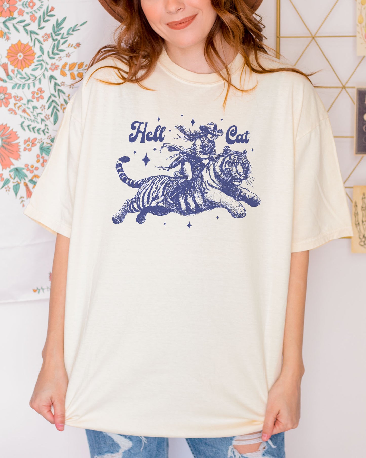 Woman wearing an ivory "Hell Cat" shirt with a retro graphic of a cowgirl riding a tiger.