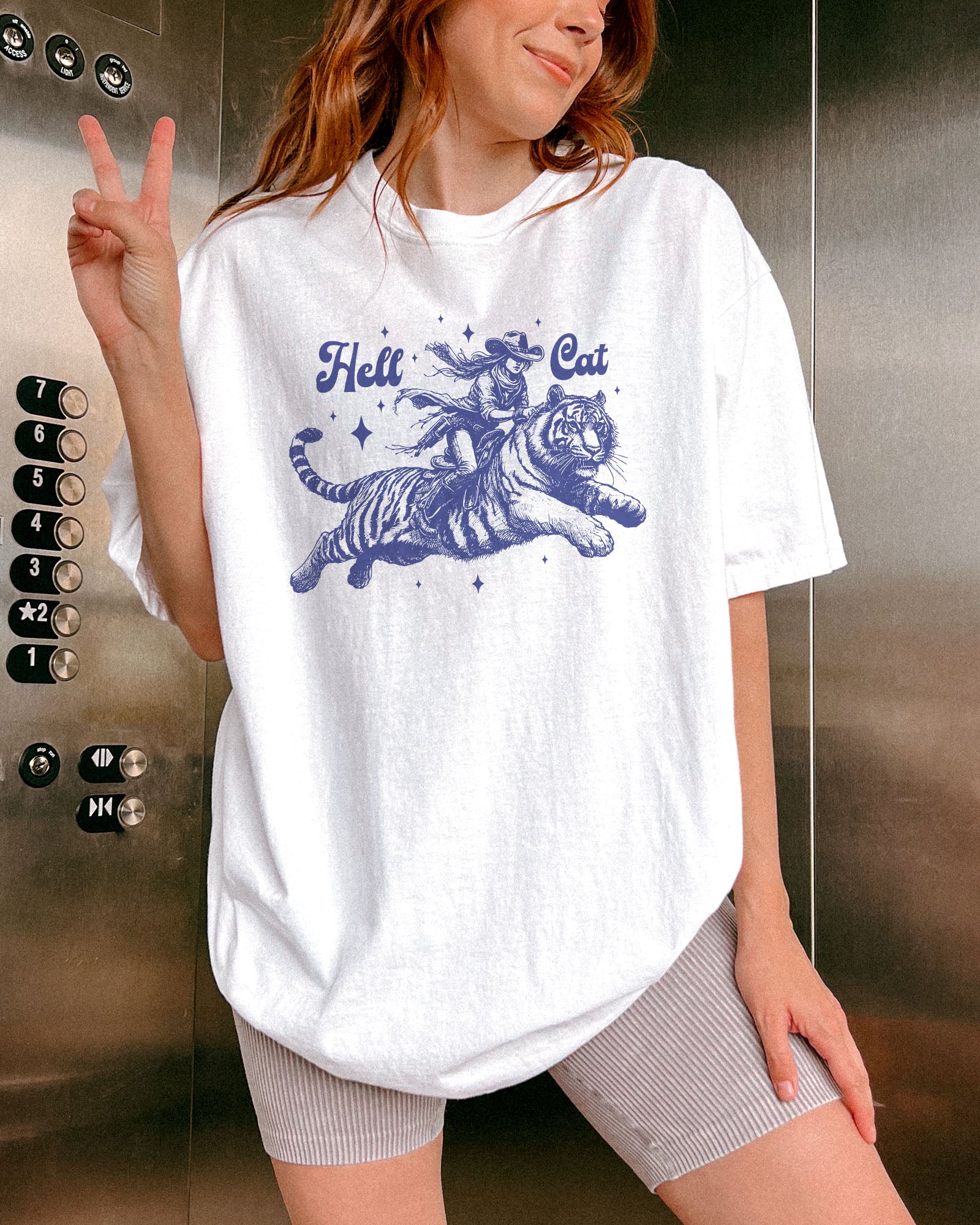 Woman wearing a white "Hell Cat" shirt with a retro graphic of a cowgirl riding a tiger.