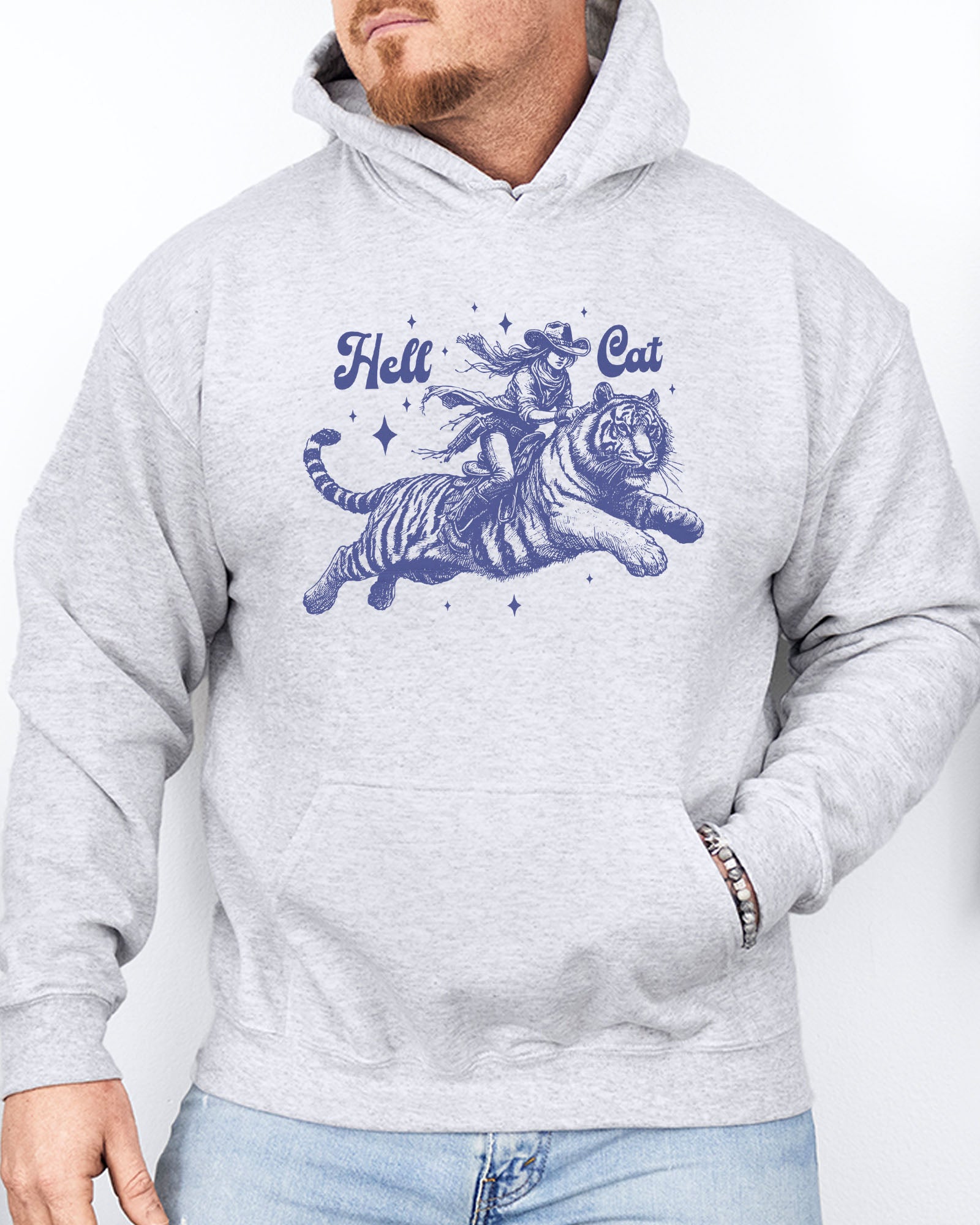 Man wearing an ash-colored hoodie featuring a retro cowgirl riding a tiger graphic, titled 'Hell Cat'.