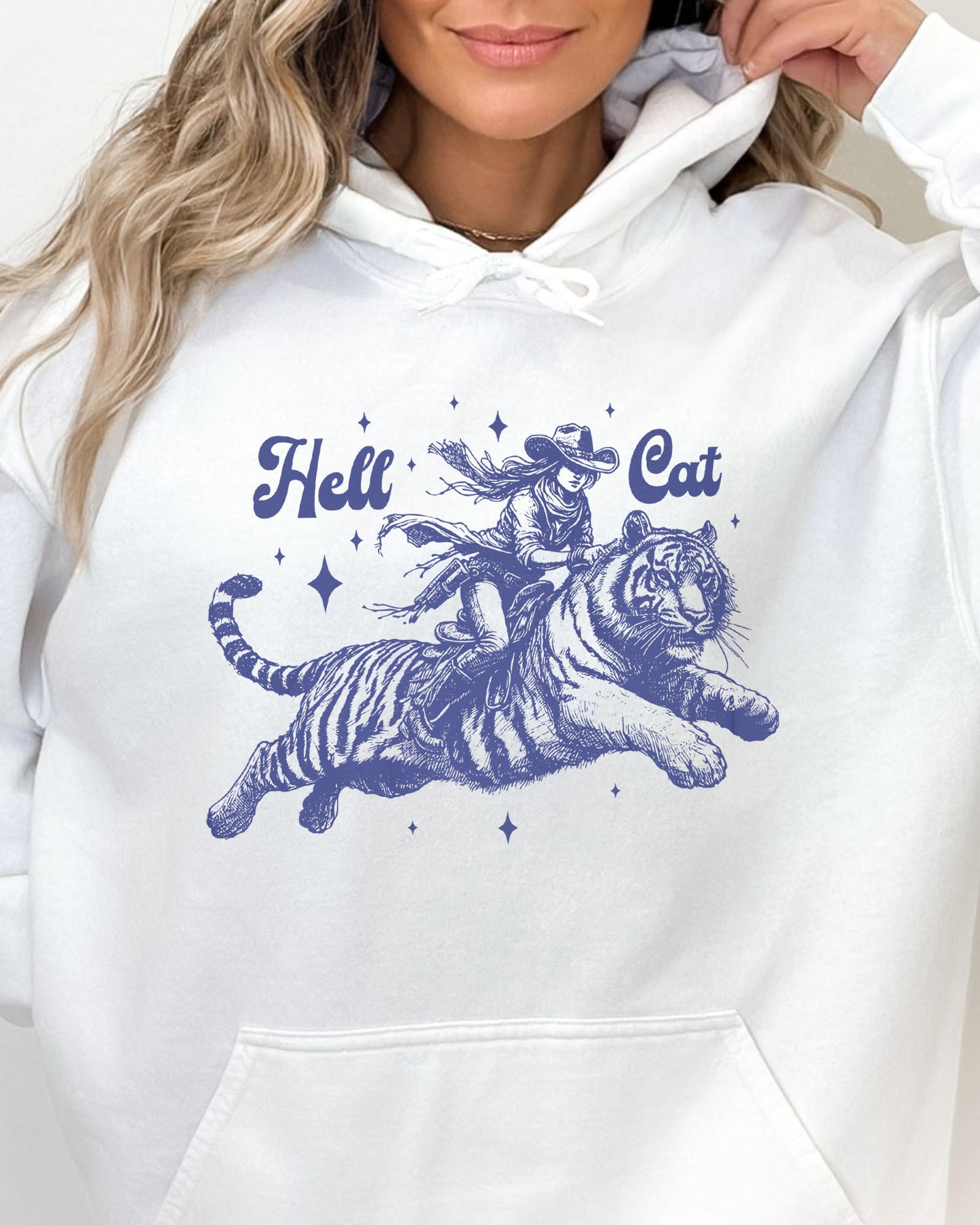 Close up of a woman wearing a white-colored hoodie featuring a retro cowgirl riding a tiger graphic, titled 'Hell Cat'.