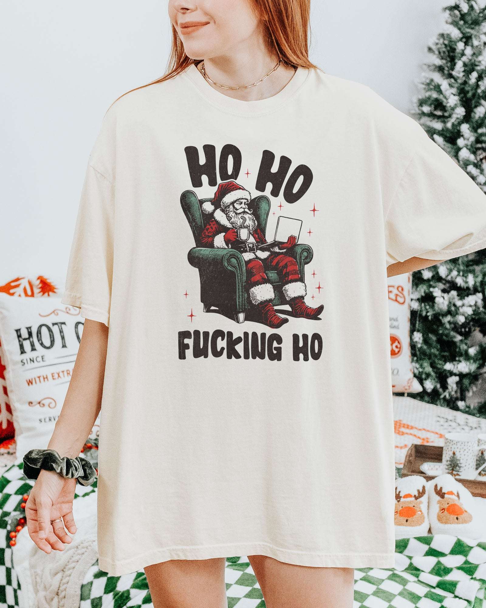 Woman wearing an ivory "Ho Ho Fucking Ho" shirt with a funny retro graphic of Santa Claus sitting in an armchair.