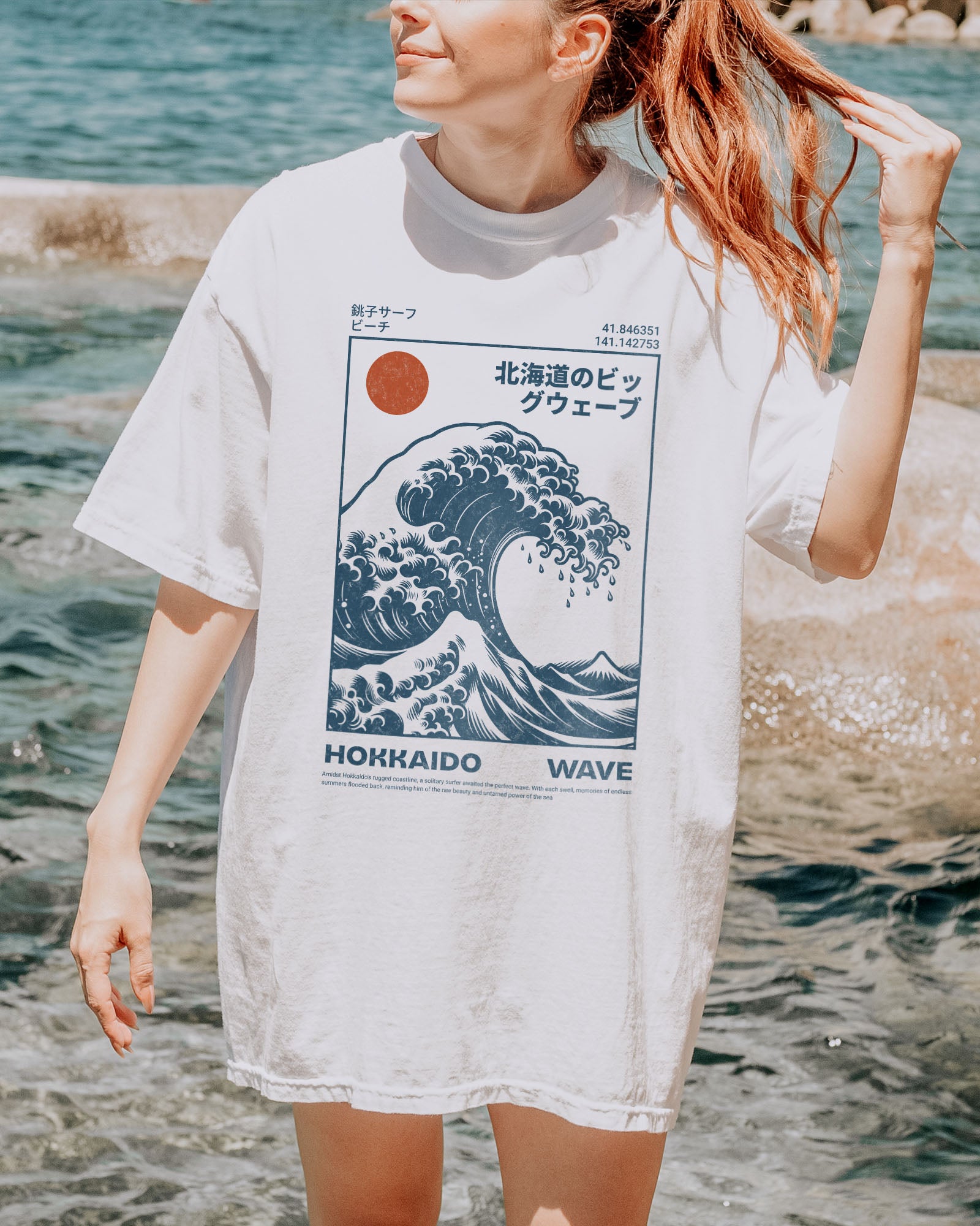 Woman on beach wearing a white ‘Hokkaido Wave’ surf shirt with a retro Japanese great wave graphic in traditional ukiyo-e style.