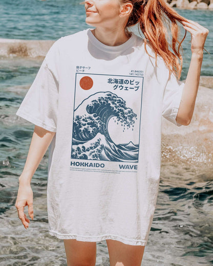 Woman on beach wearing a white ‘Hokkaido Wave’ surf shirt with a retro Japanese great wave graphic in traditional ukiyo-e style.
