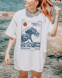 Woman on beach wearing a white ‘Hokkaido Wave’ surf shirt with a retro Japanese great wave graphic in traditional ukiyo-e style.
