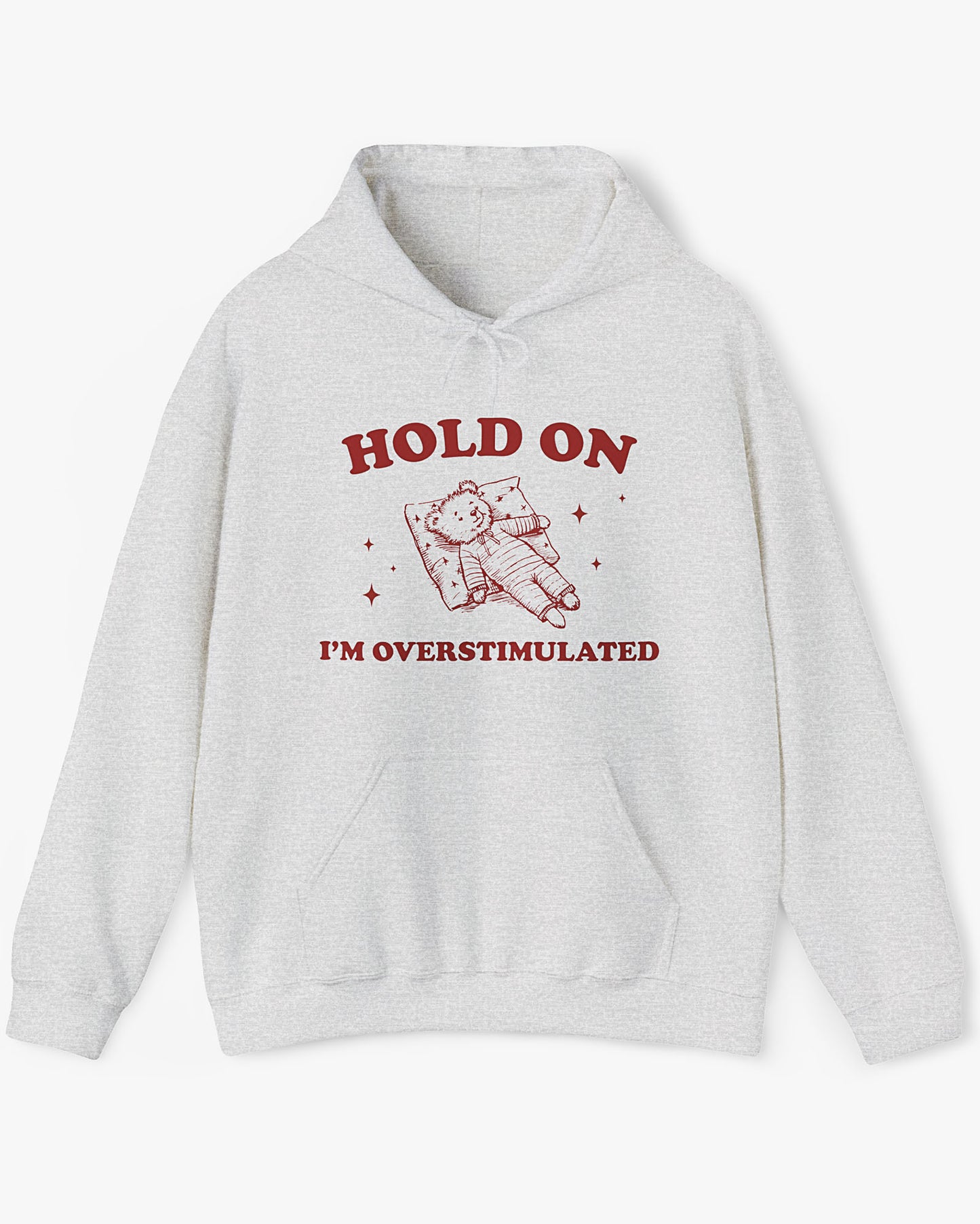 Flat lay ash gray 'Hold On I'm Overstimulated' hoodie with a retro and funny exhausted bear laying on pillow graphic