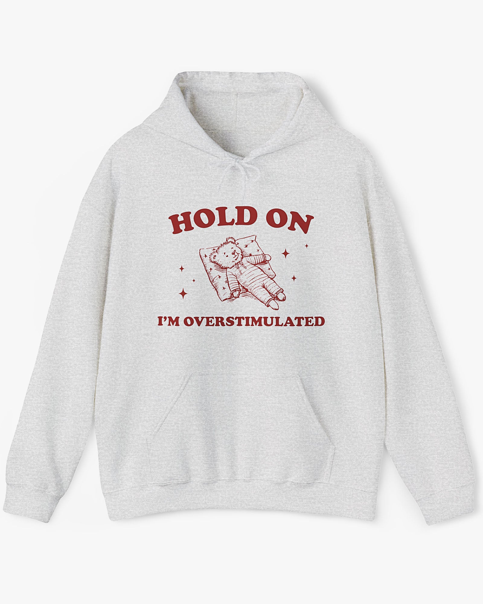 Flat lay ash gray 'Hold On I'm Overstimulated' hoodie with a retro and funny exhausted bear laying on pillow graphic