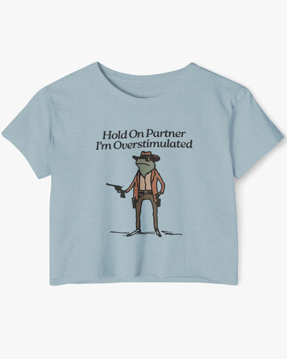 Flat lay stonewash denim 'Hold On Partner, I'm Overstimulated' crop top featuring a funny retro cowboy frog graphic.