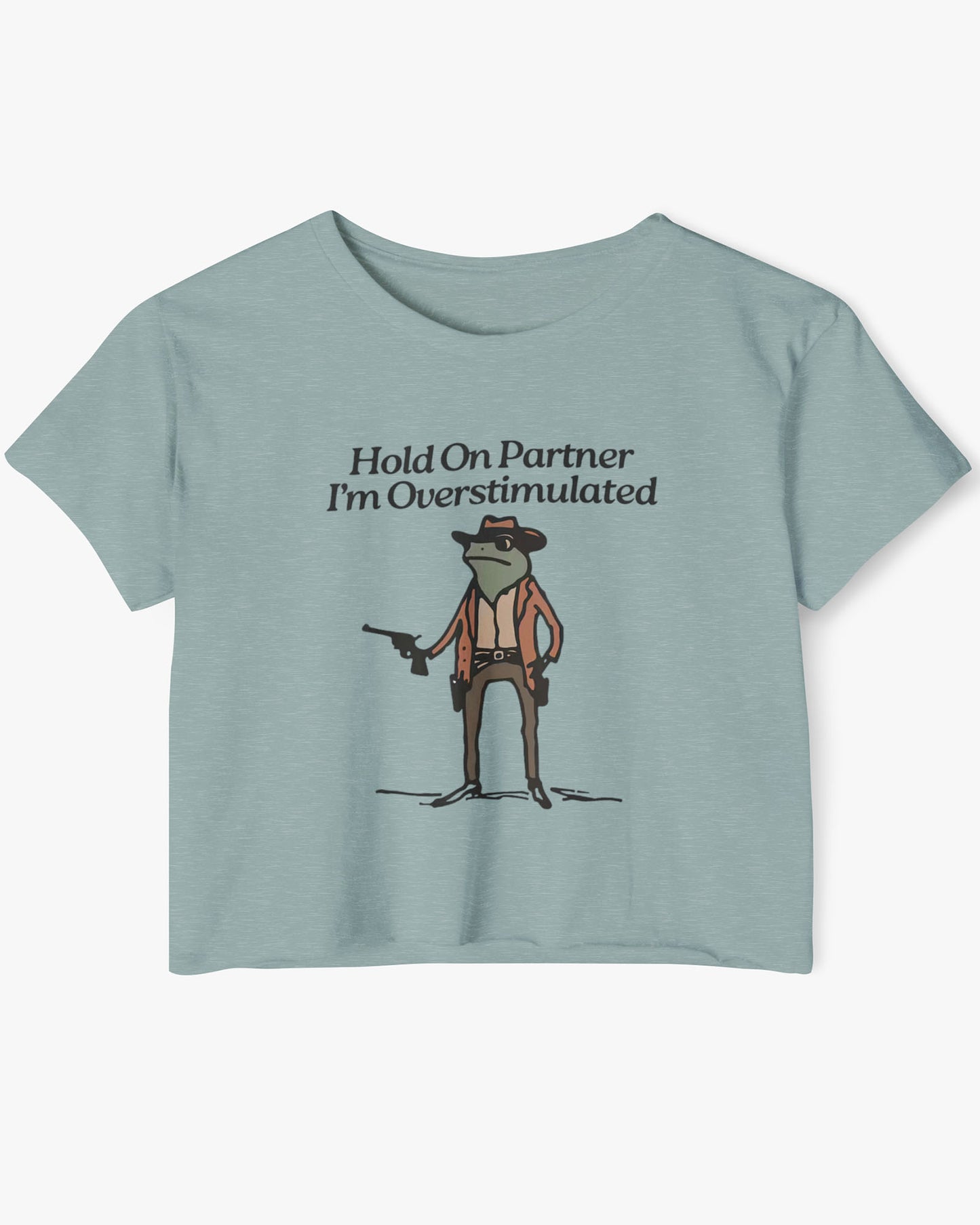 Flat lay stonewash green 'Hold On Partner, I'm Overstimulated' crop top featuring a funny retro cowboy frog graphic.